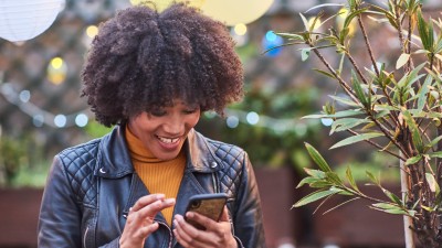 Frau mit Afrolook und mit Lederjacke bedient lächelnd Ihr Smartphone