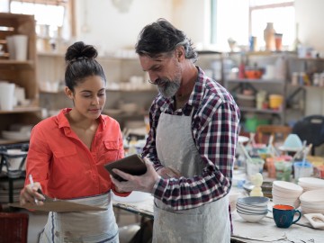 Mitarbeiter-Benefits für kleine und mittelständische Betriebe: Ein Meister erkl&auml;rt in der Werkstatt einer Angestellten etwas