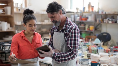Mitarbeiter-Benefits für kleine und mittelständische Betriebe: Ein Meister erklärt in der Werkstatt einer Angstellten etwas.