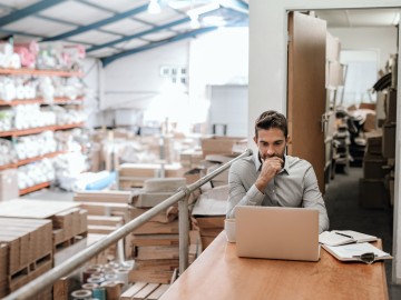 Produktsicherheitsverordnung (GPSR) 2024 - Was Unternehmen jetzt wissen müssen: Manager, der online arbeitet, während er in einem Lagerbüro sitzt 