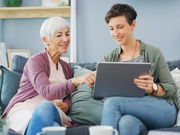 Digitaler Nachlass - Was passiert mit Online-Konten im Todesfall?: Ältere Frau und Tochter sitzen auf Sofa und besprechen etwas auf dem Tablet