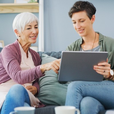 Digitaler Nachlass - Was passiert mit Online-Konten im Todesfall?: Ältere Frau und Tochter sitzen auf Sofa und besprechen etwas auf dem Tablet