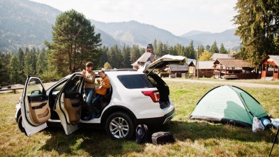Grenzenlos entspannt - So bereiten Sie Ihr Auto perfekt auf den Auslandsurlaub vor: Zwei Kinder posieren in einem Auto mit offenen T&uuml;ren auf einem Campingplatz