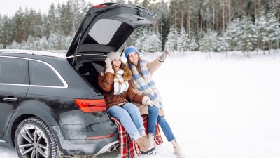 Neue Reifen-Regel - Das Alpine-Symbol kommt, die M+S-Kennzeichnung geht. : Zwei junge Frauen sitzen im Kofferraum ihres Autos in einer winterlichen Landschaft
