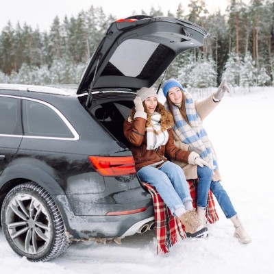 Neue Reifen-Regel - Das Alpine-Symbol kommt, die M+S-Kennzeichnung geht. : Zwei junge Frauen sitzen im Kofferraum ihres Autos in einer winterlichen Landschaft