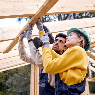 Immobilienwunsch - Wie geht es jetzt weiter?: Mann und Frau auf Baustelle bohren am Dachbalken