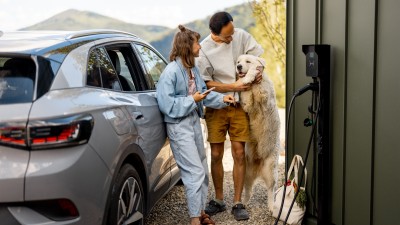 Wallbox versichern - So laden Sie Ihr E-Auto zu Hause rundum sorglos : Junges Paar mit Hund steht neben E-Auto und Wallbox
