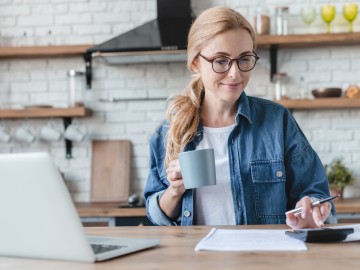 Bonus vom Fiskus - Wie Sie der Staat mit der Arbeitnehmersparzulage fürs Sparen belohnt: Frau berechnet Arbeitnehmersparzulage mit einem Taschenrechner und Laptop