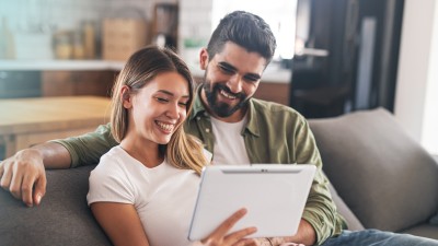 Tipps & Tricks für ein sparsames und sicheres Zuhause: Paar sitzt auf Sofa und schaut ein Tablet an