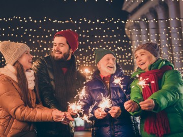 Versicherungen und Finanzen 2026 - Das ändert sich : Vier Erwachsene feiern draußen Silvester mit Lichterkerzen.