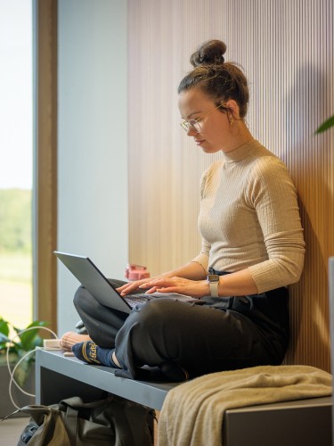 Mitarbeiterin der W&W sitzt im Schneidersitz mit ihrem Laptop auf dem Schoß auf einer Bank