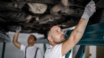 Kfz-Werkstatt: Mechaniker arbeiten an einem Unterboden