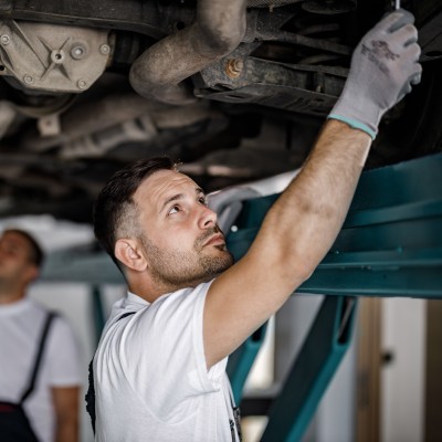 Kfz-Werkstatt: Mechaniker arbeiten an einem Unterboden