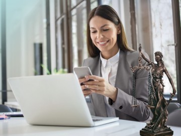 Vermögensschadenhaftpflicht: Frau in grauem Blazer sitzt mit Smartphone vor Laptop