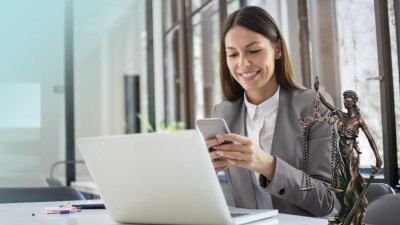 Vermögensschadenhaftpflicht: Frau in grauem Blazer sitzt mit Smartphone vor Laptop