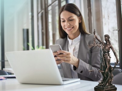 Vermögensschadenhaftpflicht: Frau in grauem Blazer sitzt mit Smartphone vor Laptop