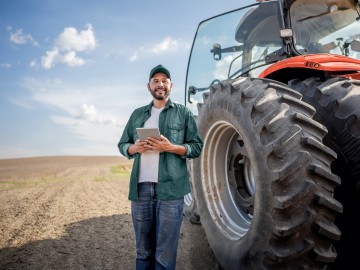 Traktor-Versicherung: Ein Landwirt mit Tablet steht vor einem Traktor