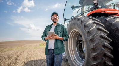 Traktor-Versicherung: Ein Landwirt mit Tablet steht vor einem Traktor