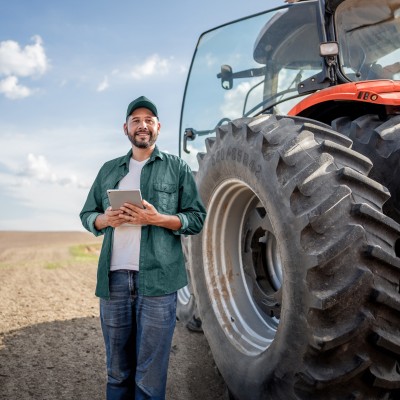 Traktor-Versicherung: Ein Landwirt mit Tablet steht vor einem Traktor