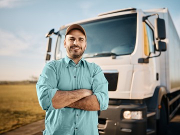 LKW-Versicherung: Lkw-Fahrer steht mit verschränkten Armen vor seinem Lastkraftwagen