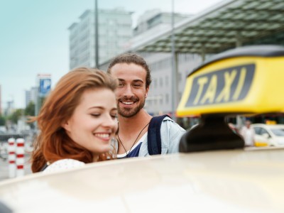 Taxiversicherung: Ein Paar hinter einem Taxischild auf einem Fahrzeug.