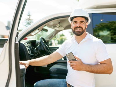 Flottenversicherung: Mann mit Smartphone steigt in ein Auto