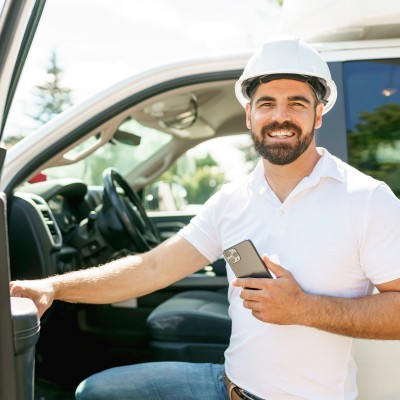Flottenversicherung: Mann mit Smartphone steigt in ein Auto
