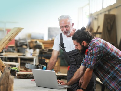 Gebäudeversicherung für Ihr Gewerbe: Zwei Handwerker in der Schreinerei am Laptop