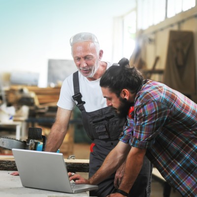 Gebäudeversicherung für Ihr Gewerbe: Zwei Handwerker in der Schreinerei am Laptop