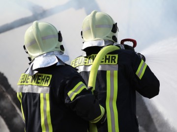 Zwei Feuerwehrmänner halten einen Wasserschlauch und sprühen Wasser