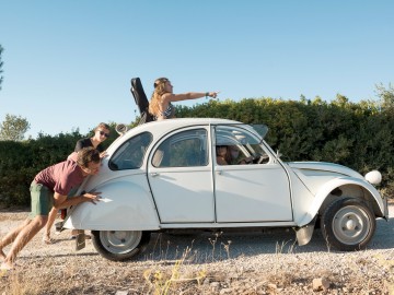 Eine nostalgische Reise durch die Geschichte der Kfz-Versicherung: Junge Leute schieben eine Citroen 2CV-Ente auf einem Kiesweg 