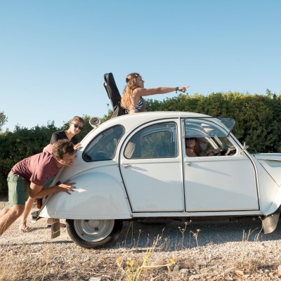 Eine nostalgische Reise durch die Geschichte der Kfz-Versicherung: Junge Leute schieben eine Citroen 2CV-Ente auf einem Kiesweg 