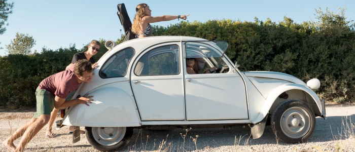 Junge Leute schieben eine Citroen 2CV-Ente auf einem Kiesweg 
