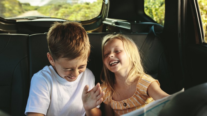 Zwei junge Geschwister lachend auf der Rückbank eines Fahrzeugs