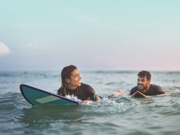 Junge Frau und Mann im Neoprenanzug und Surfbrett im Wasser