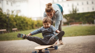 Haftpflichtversicherung für Familien: Mutter schiebt Kind auf dem Skateboard an