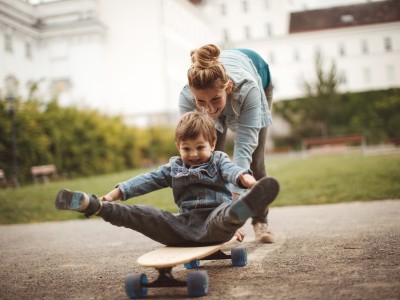 Haftpflichtversicherung für Familien: Mutter schiebt Kind auf dem Skateboard an