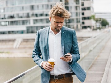Geschäftsmann mit Smartphone und Kaffebecher zu Fuß unterwegs