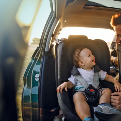 Verkehrsrechtsschutz: Junger Vater ist mit seinem Kind auf der Rückbank seines Auto und lächelt dieses an