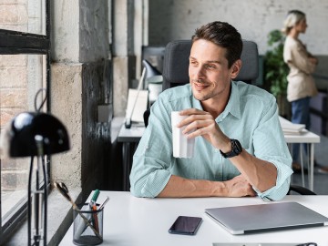 Mann sitzt im B&uuml;ro an seinem Schreibtisch mit einem Trinkbecher in der Hand