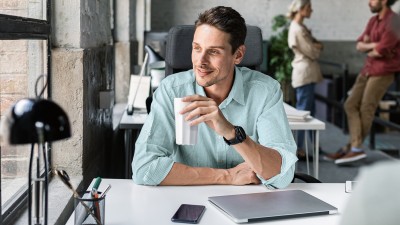 Mann sitzt im B&uuml;ro an seinem Schreibtisch mit einem Trinkbecher in der Hand