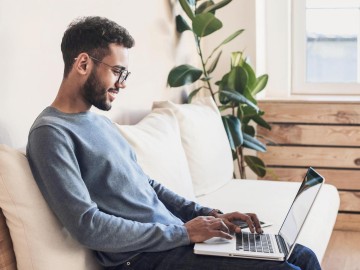Mann im Homeoffice sitzt mit dem Laptop auf dem Sofo