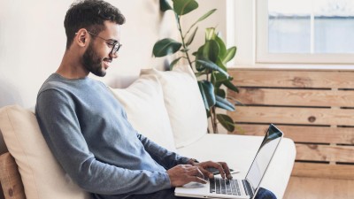 Mann im Homeoffice sitzt mit dem Laptop auf dem Sofo