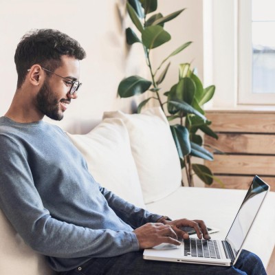Mann im Homeoffice sitzt mit dem Laptop auf dem Sofo
