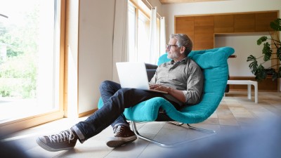 Mann gemütlich mit Laptop in einem großen Liegesessel 