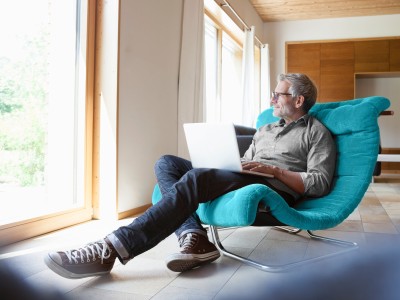 Mann gemütlich mit Laptop in einem großen Liegesessel 