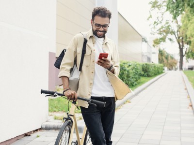 Mann schiebt sein Fahrrad und schaut auf sein Smartphone