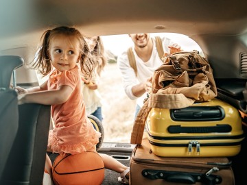 Auslandsreisekrankenversicherung: Vater mit Tochter auf gepackten Koffern freuen sich auf Ihren Urlaub