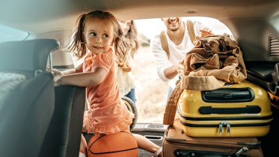 Auslandsreisekrankenversicherung: Vater mit Tochter auf gepackten Koffern freuen sich auf Ihren Urlaub