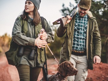 Jagdhaftpflichtversicherung: Junge Frau und Mann laufen mit ihrem Hund im Wald